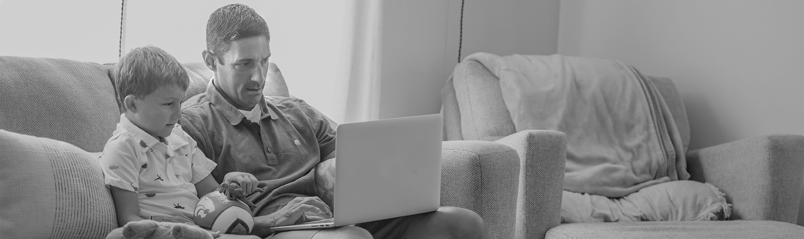 Online student sitting with child on couch using a laptop to work on online courses